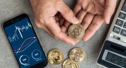 Hand holding physical bitcoins with a phone and calculator visible